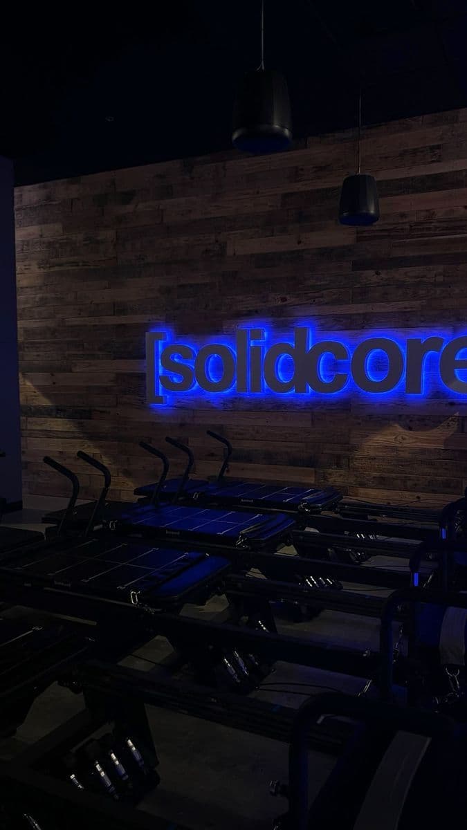 El letrero de solidcore iluminado en azul sobre una pared de madera y filas de reformers.